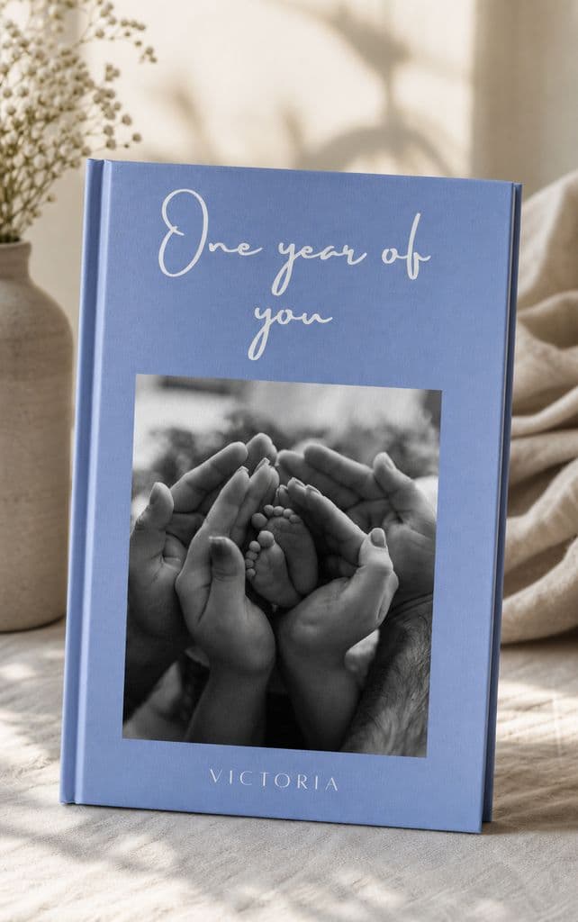 Álbum del primer año en tapa dura azul, con las manos de la familia sosteniendo los pies del bebé